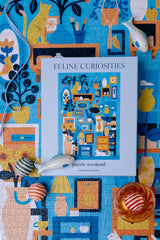 Feline Curiosities puzzle packaging on a colorful background with cat-themed illustrations.