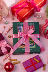 Gift box with pink ribbon surrounded by festive decorations on a pink surface