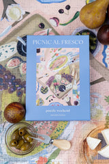 Jigsaw puzzle box titled 'Picnic al Fresco' on a partially completed puzzle with fruits and vegetables.